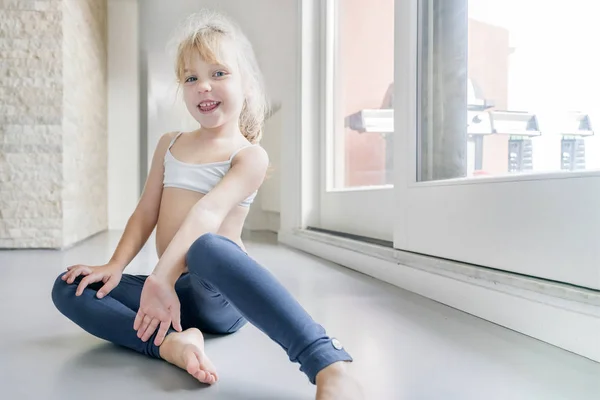 Happy Little Blond Girl White Top Blue Leggings Sitting Floor — ストック写真