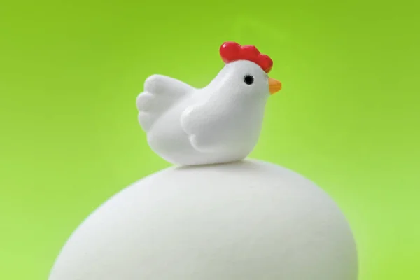 Little toy chicken sitting on a big white egg on a green background
