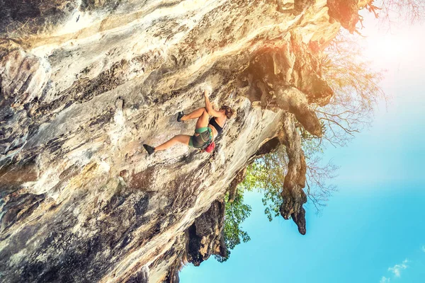 A woman climber climbs a cliff without safety equipment on a sunny day