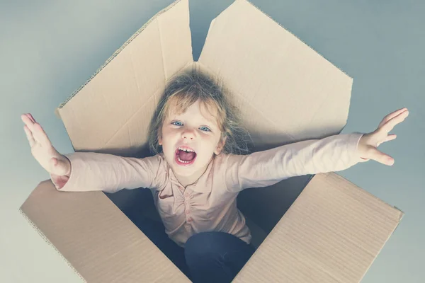 Llittle blue-eyed blonde girl screams inside a cardboard box. Toned