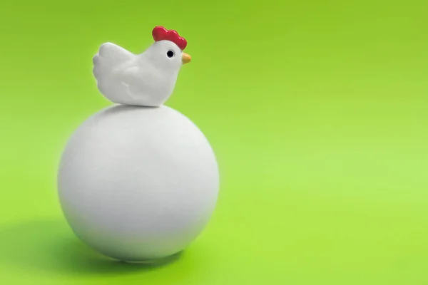 Little toy chicken sitting on a big white egg on a green background
