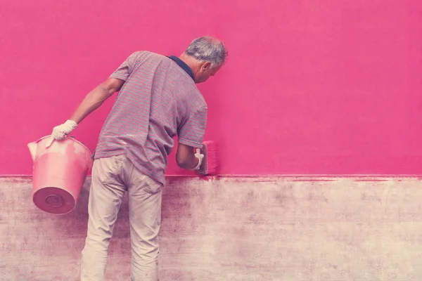 一个用水桶画墙的人用粉红色 — 图库照片