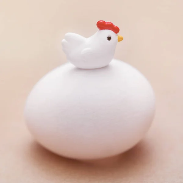 Little toy chicken sitting on a big white egg on a pink background