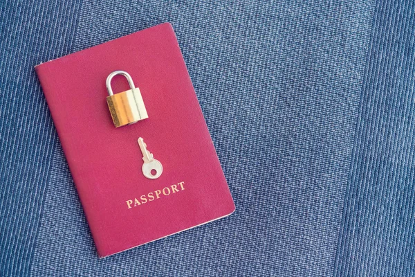 Golden lock and key lying on the red passport on a blue textile background, close-up