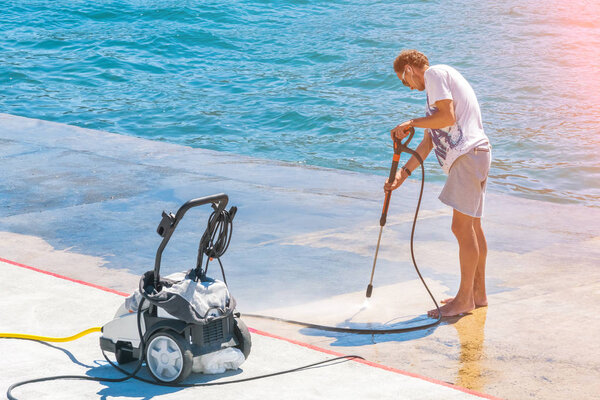 Kotor, Montenegro, April 28, 2017:  Young man with high-pressure cleaners for cleaning washes quay in the sunlight