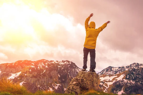 彼の手で岩の上に立って 後ろ姿で夕日を見てフード付き黄色のジャケットの男 — ストック写真
