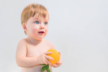 Sürpriz mavi gözlü bebek gri bir arka plan üzerinde bir portakal tutan