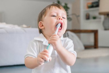 Sevimli küçük mavi gözlü sarışın çocuk diş fırçası ile dişlerini fırçalıyor beyaz polo gömlek