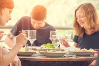 İnsanlar güneş ışığında terasta yemek yiyip şarap içiyorlar.