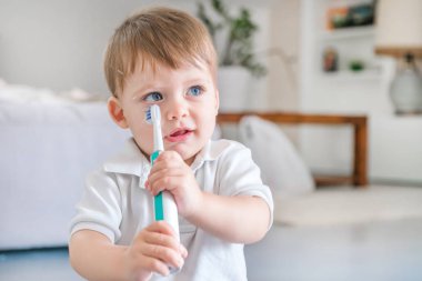 Küçük mavi gözlü sarışın çocuk odasında bir diş fırçası ile dişlerini fırçalıyor beyaz polo gömlek