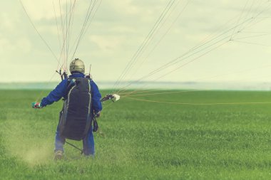 Yamaçparaşütü üzerinde yeşil bir alana iniş sırasında adam. Tonda