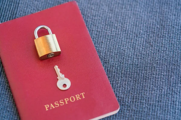 金锁和钥匙躺在红色护照上的蓝色纺织品背景 — 图库照片