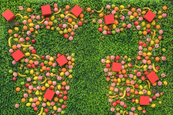 Letter T made of red cubes and fruits on the green grass, background