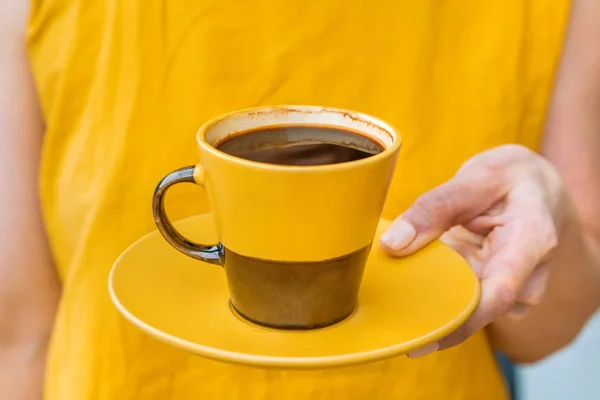Woman in yellow clothes is holding a yellow and brown mug with coffee