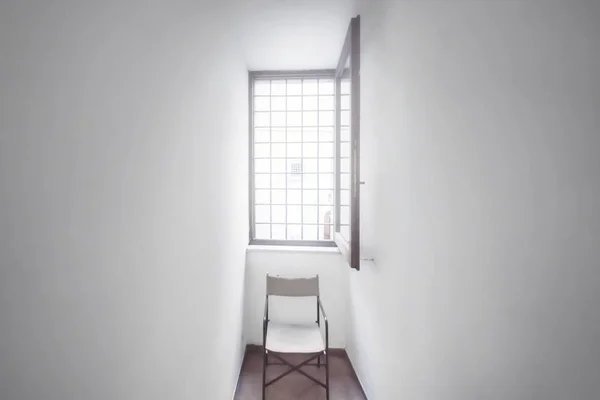 A small white room with a window and an empty chair