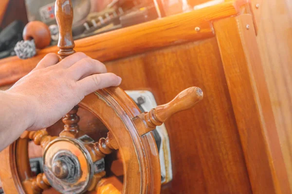 captain\'s hand holds a wooden ship\'s helm