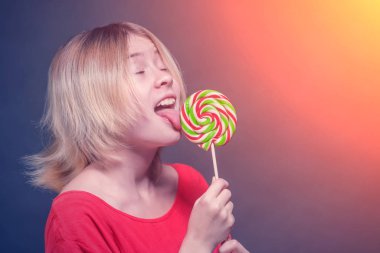 sarışın kız Genç kırmızı bir bluz içinde güneş ışığı altında lolipop yalıyor