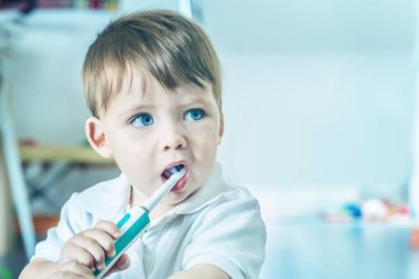 Sevimli küçük mavi gözlü sarışın çocuk diş fırçası ile dişlerini fırçalıyor beyaz polo gömlek