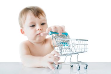 Sevimli küçük sarışın çocuk beyaz bir arka plan üzerinde masada küçük bir alışveriş arabası ile çalış