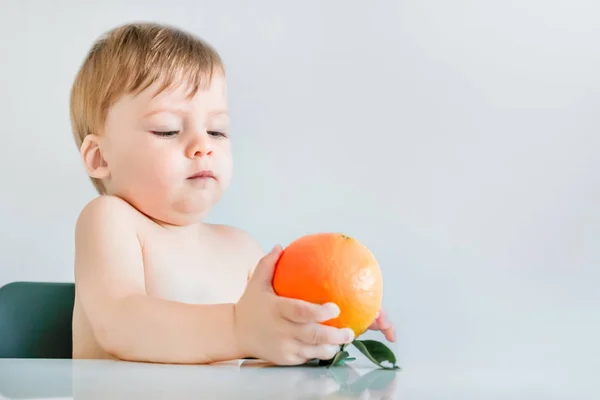 Lindo Niño Rubio Pequeño Sentado Mesa Sosteniendo Una Naranja —  Fotos de Stock