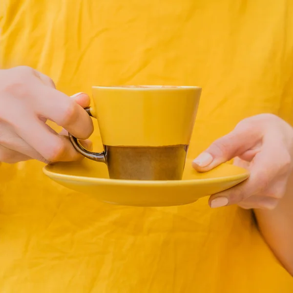 Woman in yellow clothes is holding a yellow and brown mug with coffee