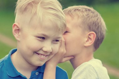 Sarışın çocuk kulağına arkadaşı konuşuyor.