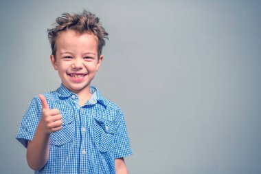 Mavi gömlekli başparmak gri bir arka plan üzerinde gösterilen boy gülümseyerek