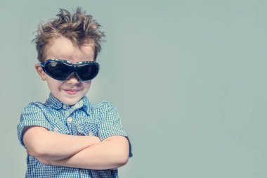 Mavi gömlekli gülümseyen yakışıklı eller ve güneş gözlüğü göğsünde gri bir arka plan üzerinde çarpı işareti