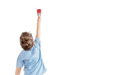 Mavi gömlekli çocuk molar fırça beyaz bir duvar bir kırmızı boya ile boyar. İzole