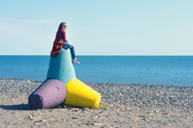 Sahilde bir beton tetrapod üzerinde oturan kadın