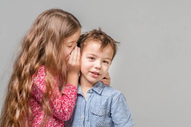 Kırmızı bir bluz, küçük kız mavi gömlekli bir çocuğun kulağına fısıldar