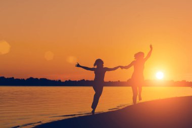 Gün batımında sahilde çalıştıran elele bir kadın silüeti