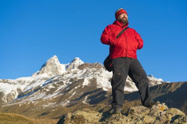 Sakallı adam dağın tepesinde kırmızı ceket ayakta