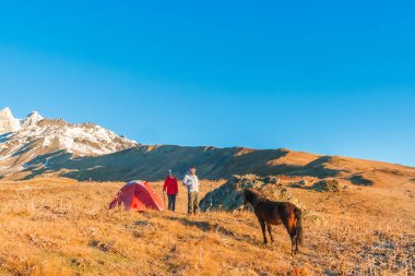 Kadın ve adam yanındaki dağlarda at bakarak bir kırmızı çadır