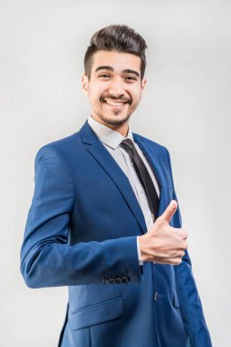 Gri bir arka plan üzerinde başparmak gösterilmesini mavi elbiseli Genç çekici adam. İzole