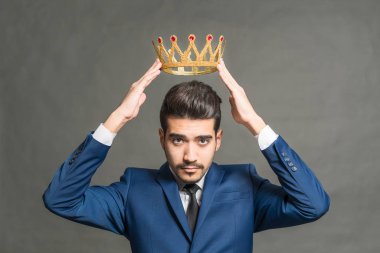 Başını altın bir taç gri bir arka plan üzerinde tutan mavi elbiseli Genç çekici adam