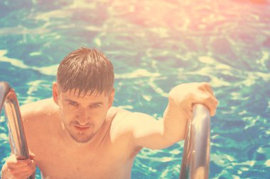 Yakışıklı ıslak adam havuzun güneş ışığı altında merdivenlerden tırmanıyor