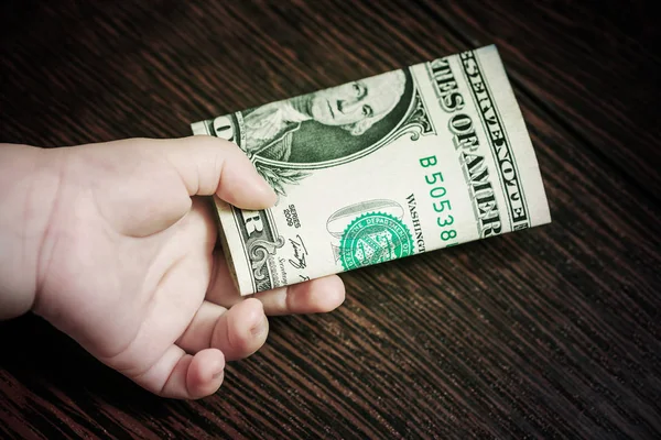 Dollars bundle in the hand of a baby on a wooden background