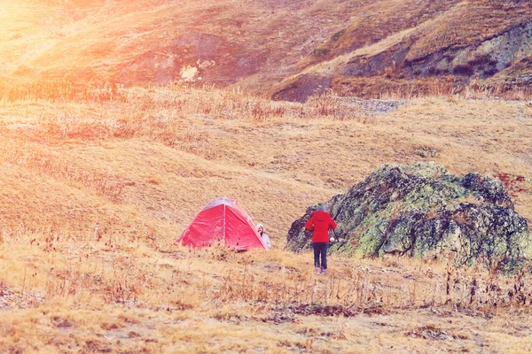 People near a red tourist tent in the mountains at sunny day