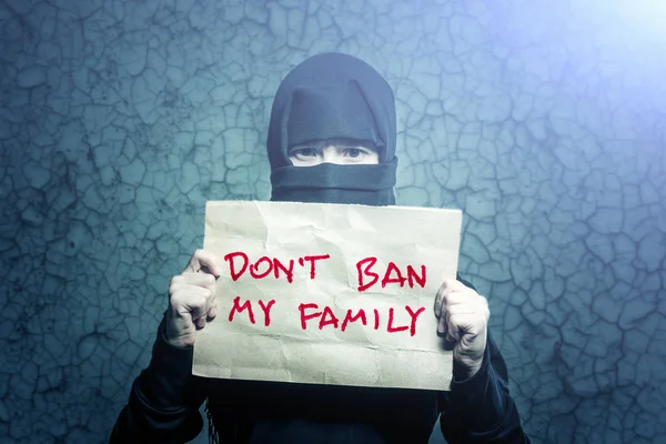 穆斯林女孩在黑色头巾拿着一张海报与题字不要禁止我的家人在背景墙上与裂缝 — 图库照片