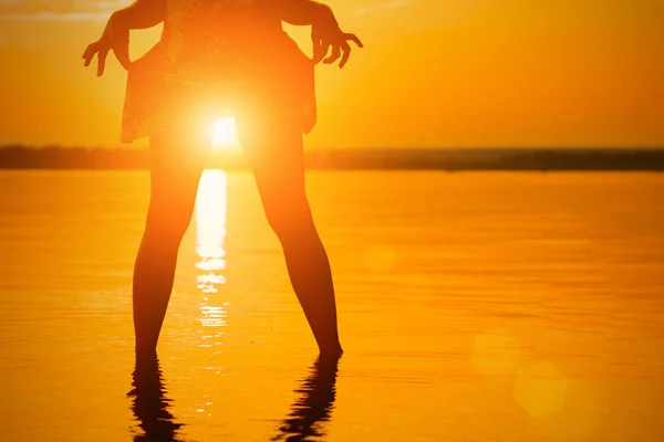 Silhouette of the woman with the sun between the legs in the water at sunset