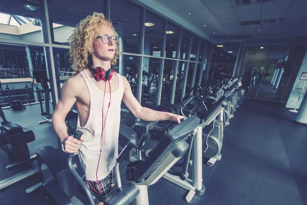 Curly blond guy with glasses and red headphones on the treadmill