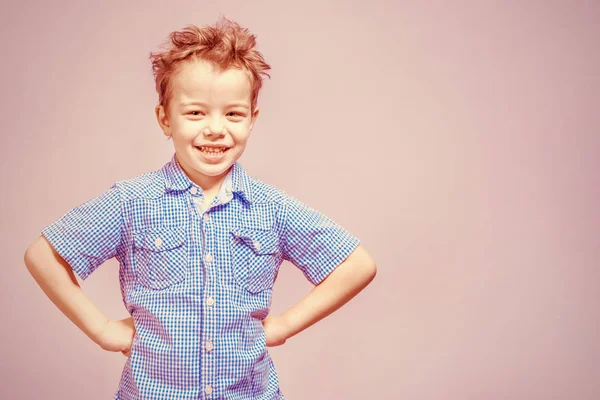 可爱的小男孩在蓝色衬衫站在他的手在他的臀部粉红色的背景 — 图库照片