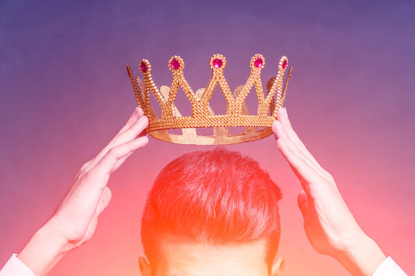 Man brunette holding above his head a golden crown  in the bright glow