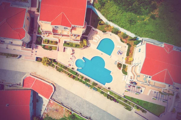 Top view of people lying on a deckchair by the pool and a house with red tiled roofs. Toned