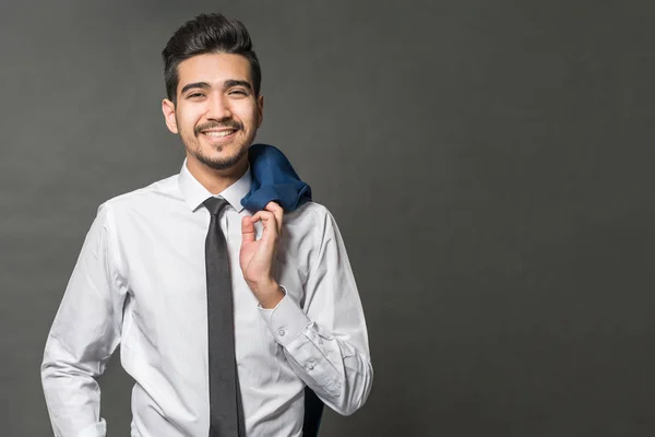 Young attractive man in a white shirt, tie and jacket hanging on his shoulder on a gray background