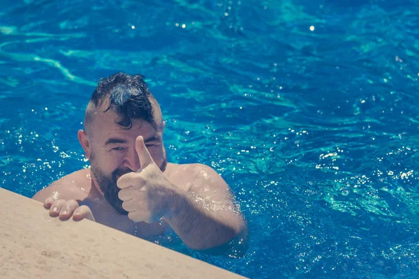 Bearded man with a a mohawk hairstyle showing hand gesture cool in the pool