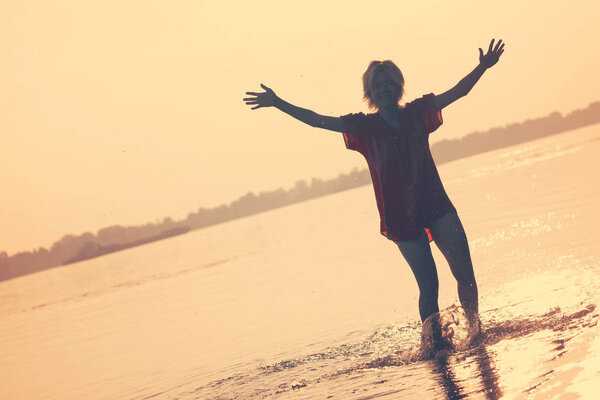 Girl teenager standing in the water with a raised hands at sunset