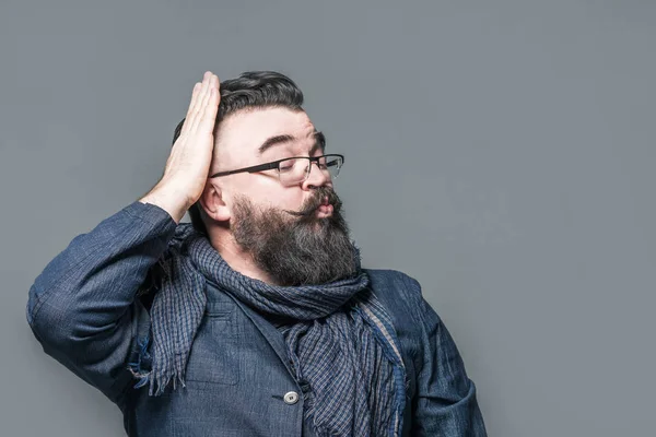 Narcissistic adult bearded man in a scarf and glasses corrects hair with hand on a gray background. Isolated