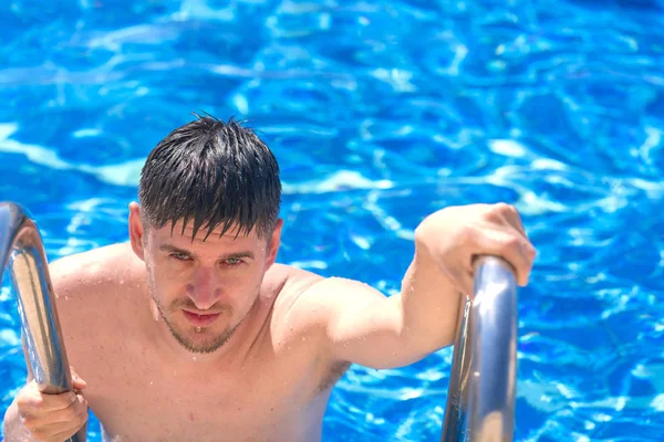 Handsome wet man climbs the stairs to the pool